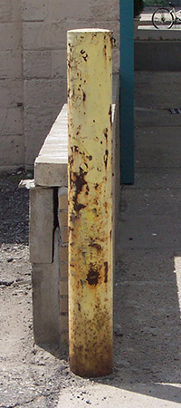 Rusty yellow bollard before a bollard cover